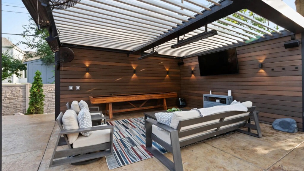 Modern aluminum pergola with wood accent wall, patio seating, and mounted outdoor TV.