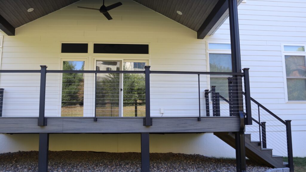 Modern elevated deck with black aluminum cable railing and gray composite decking in backyard.