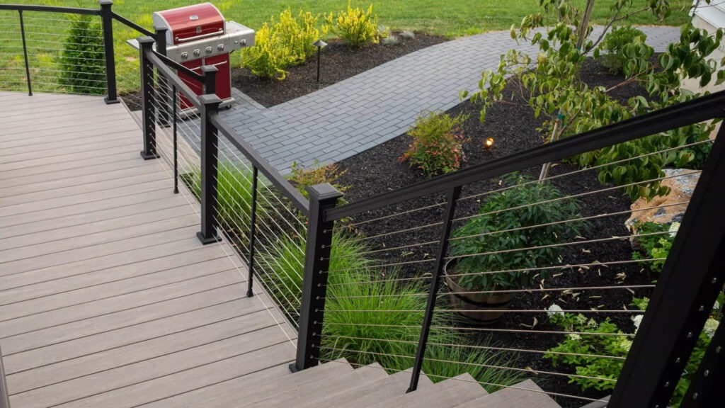 Black aluminum cable deck railing with stainless steel cables surrounding backyard greenery, elegant example of cable deck railing ideas for modern outdoor decks.