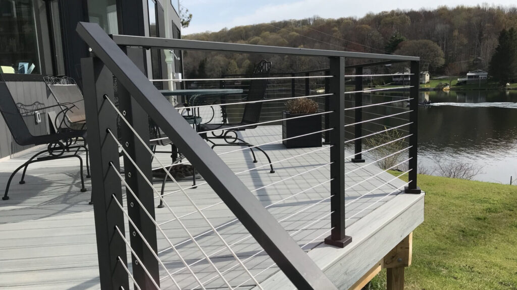 Black aluminum cable railing on gray composite deck overlooking a lake, sleek example of cable deck railing ideas for outdoor spaces.
