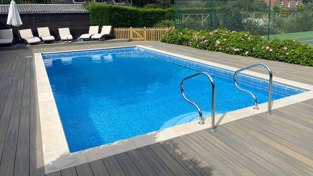 Gray composite deck surrounding a rectangular blue inground pool with lounge chairs.