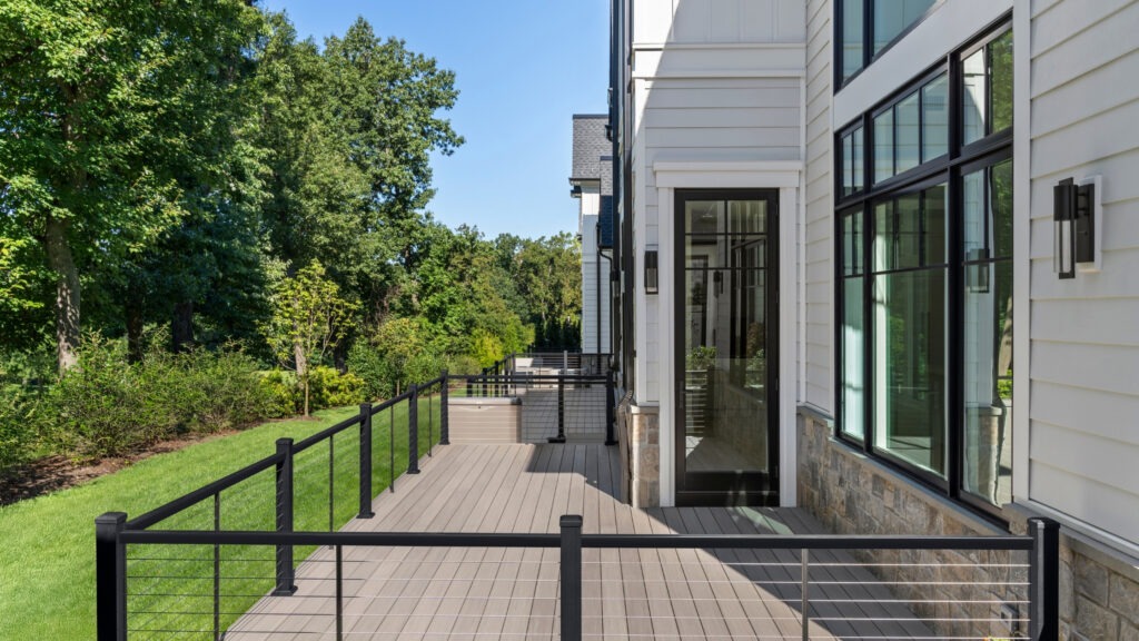 Modern gray TimberTech AZEK deck with black cable railing beside white board-and-batten siding.