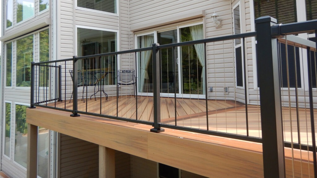 Modern balcony deck with black frame and vertical stainless cable railing near large windows.