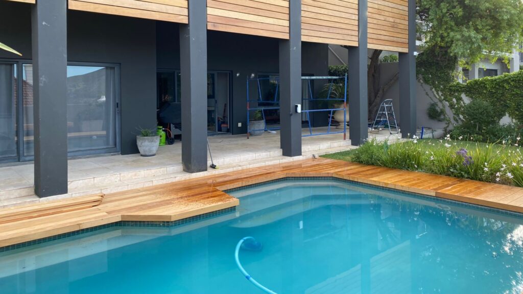 Modern inground pool with wooden step decking and dark exterior pillars.