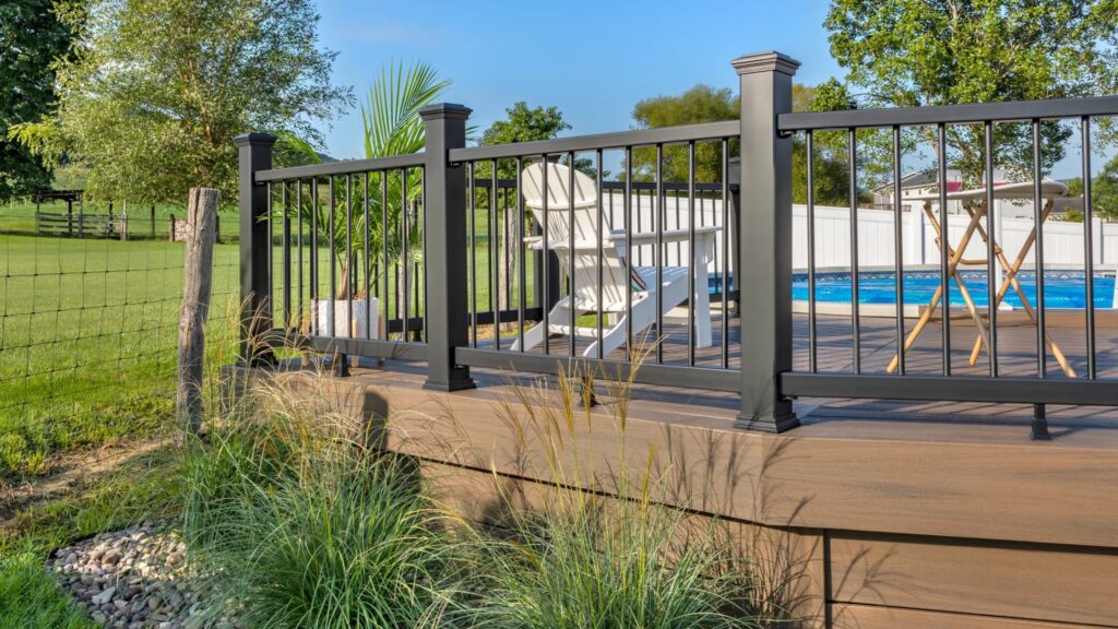 Modern composite pool deck with black railings, brown decking, and open backyard view.