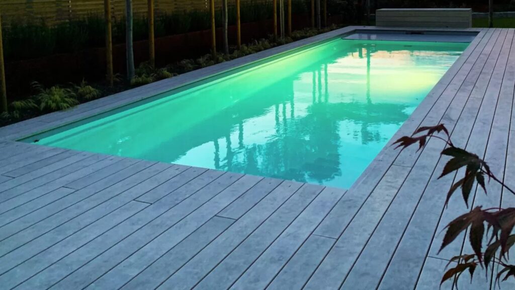 Modern rectangular above-ground pool deck with gray boards and glowing night lighting.