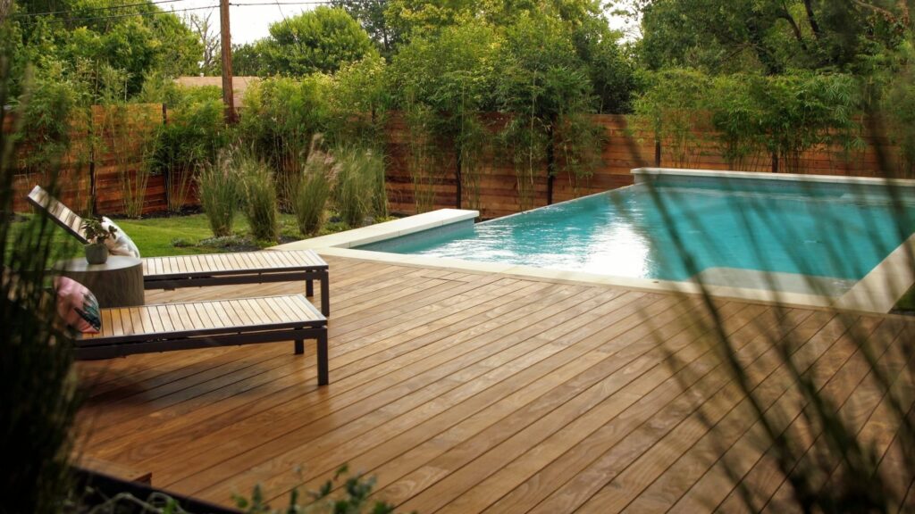 Modern wooden pool deck with lush plants and warm natural finish.