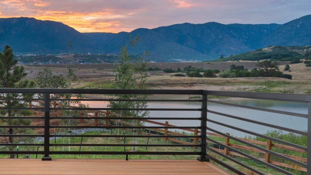 Black horizontal metal deck railing with panoramic mountain and lake view during sunset.