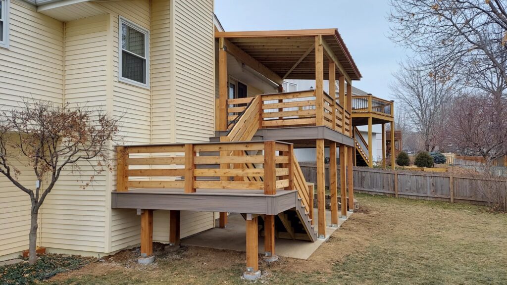 Multi-level cedar deck with horizontal wood railing and covered upper section attached to beige house.