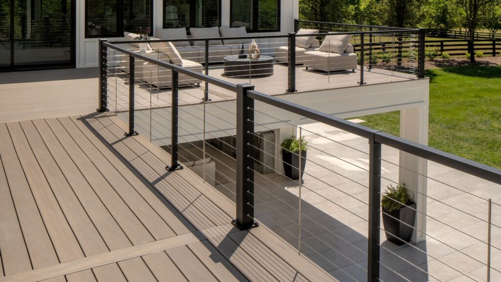 Multi-level composite deck with stainless steel cable railing and modern black aluminum posts.
