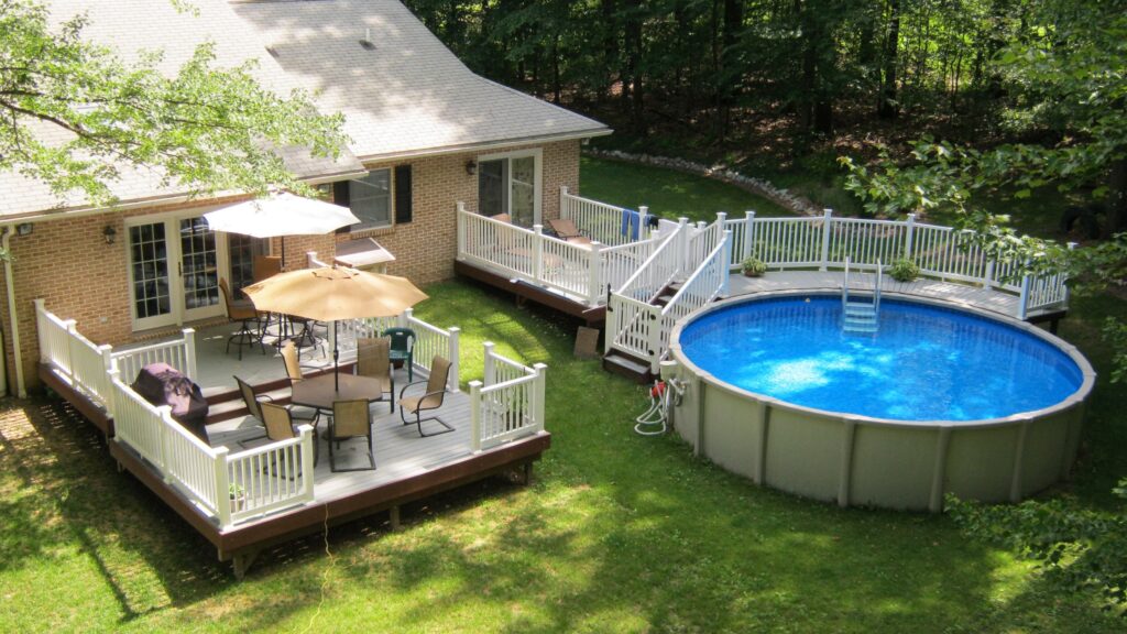 Multi-level above ground pool deck with white railings, outdoor seating, and wooden flooring.