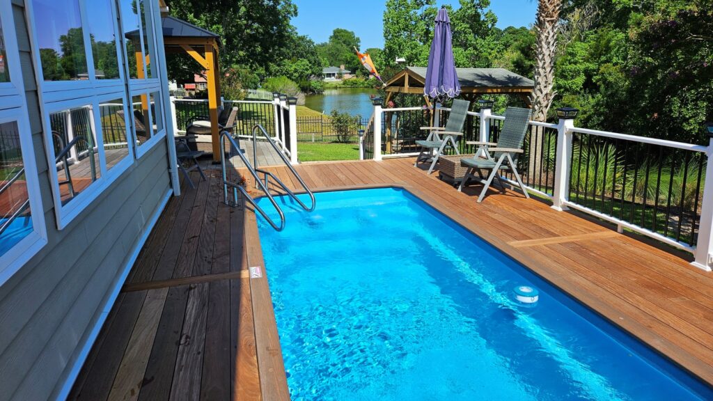 Above ground pool with narrow wood deck, white railing, and lake view in the background.