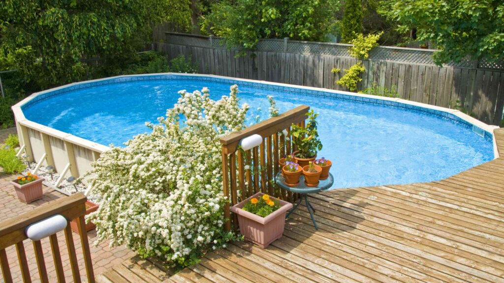 Natural wood pool deck with flowering bushes and potted plants in sunny backyard.