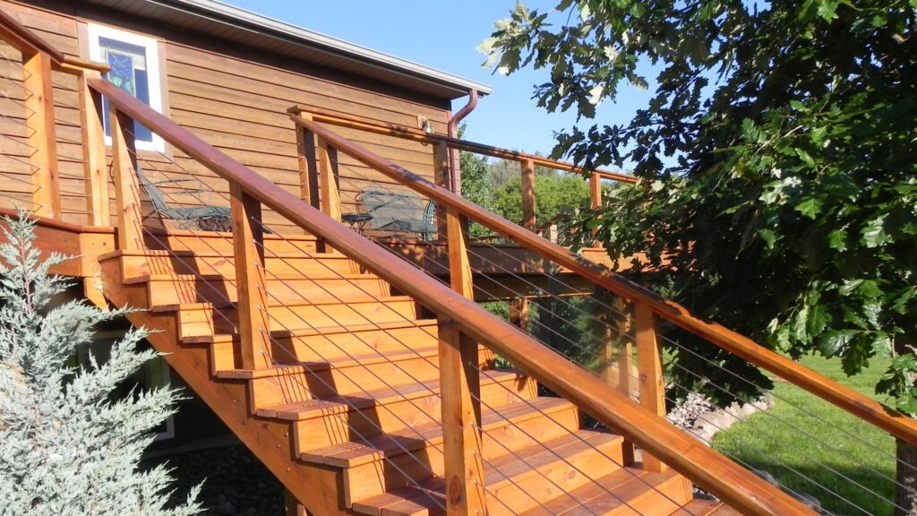 Horizontal wood and stainless-steel stair railing with modern cable design for outdoor deck stairs.