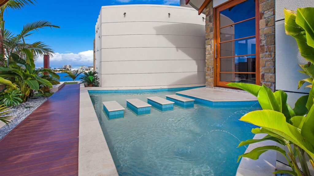 Modern pool with floating concrete steps and tropical plants overlooking waterfront.