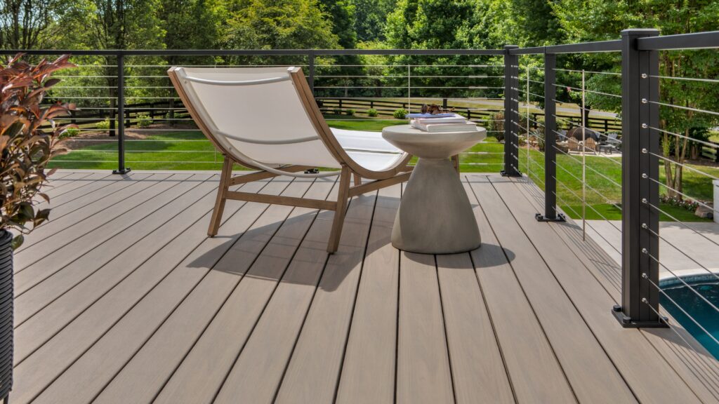 Poolside deck with black horizontal cable railing and light brown composite decking overlooking green lawn.