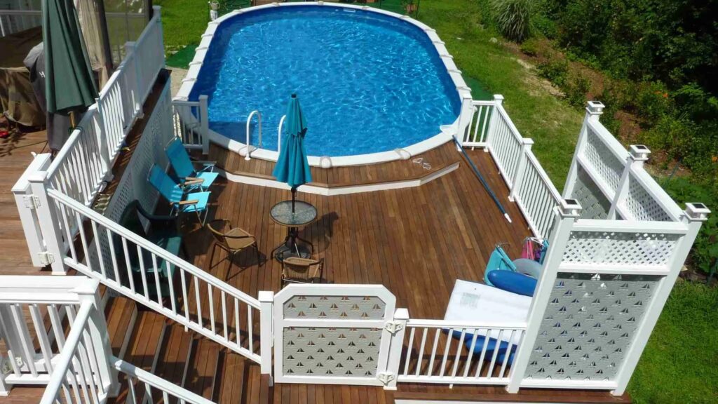Raised above ground pool deck with wooden floor and white railings near a home exterior.