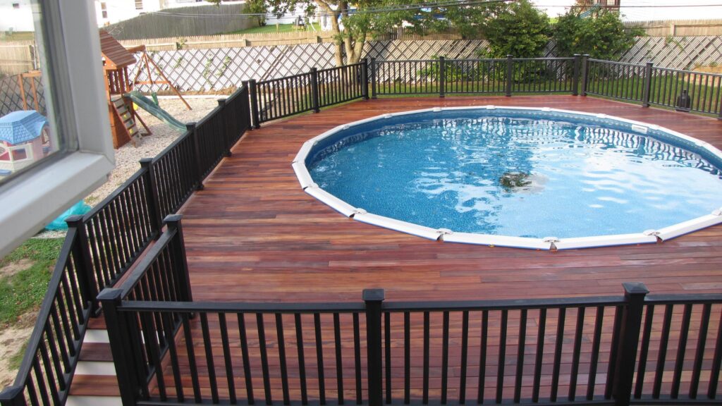 Circular pool deck with rich brown wood boards and black safety railing.