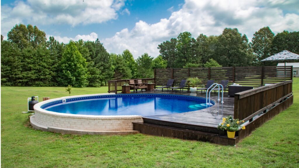 Circular inground pool with dark wood decking and privacy fence in open yard.