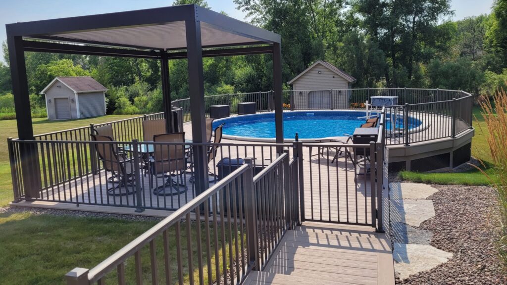 Round above ground pool deck with black railings, modern pergola, and patio chairs.