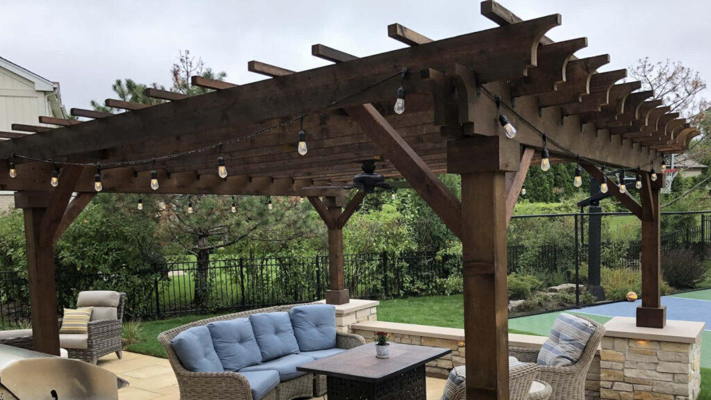 Rustic dark wood pergola with hanging string lights and wicker furniture on patio.