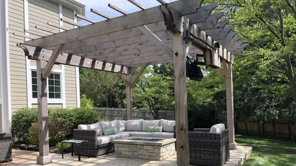 Rustic gray wooden pergola with stone firepit and wicker sectional in backyard patio.