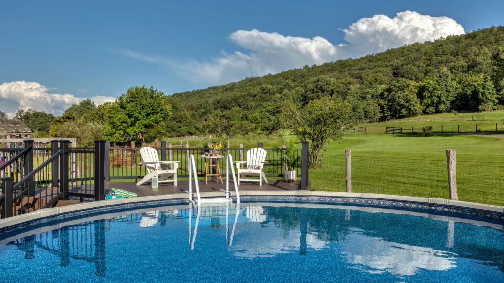 Scenic above ground pool deck with black railings, Adirondack chairs, and countryside backdrop.