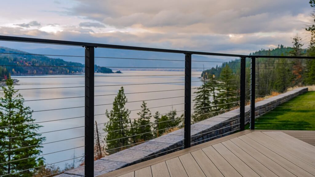 Modern horizontal black cable deck railing with aluminum posts overlooking mountain lake and forest view.