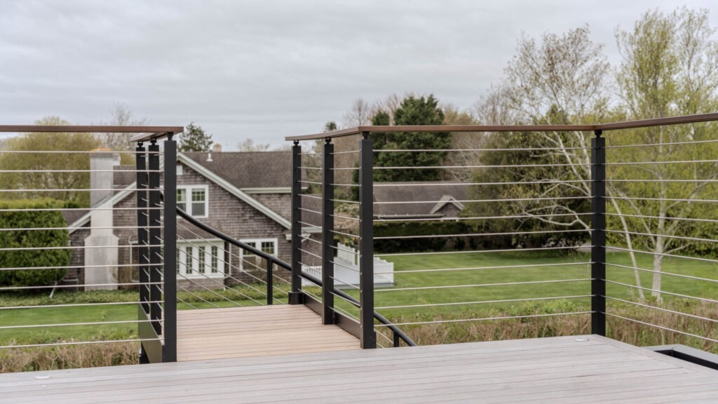 Black spiral staircase with horizontal cable railing leading to composite deck, creative example of cable deck railing ideas for multi-level spaces.
