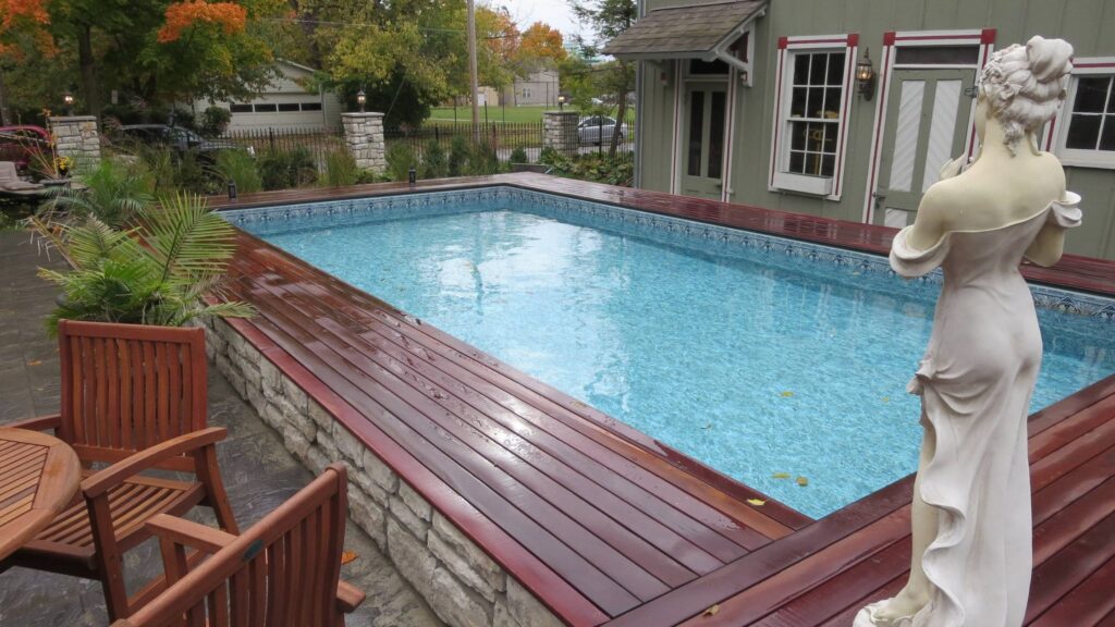 Above ground pool deck with wood trim, stone base, and decorative statue.