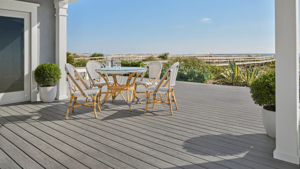 TimberTech Driftwood Reserve deck with rattan dining chairs and coastal beach background.