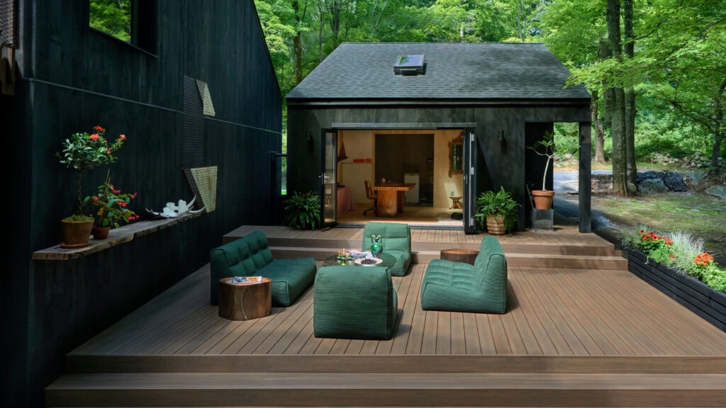 TimberTech English Walnut deck with dark siding, green furniture, and lush forest view.