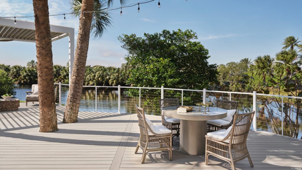 Tropical outdoor deck with white aluminum cable railing gray composite boards and palm trees near water.