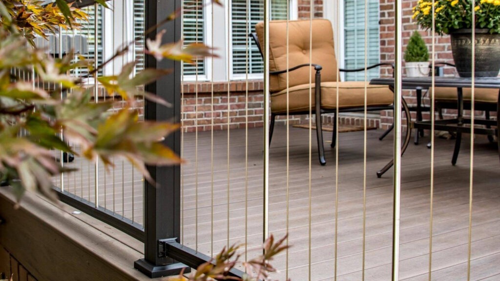 Vertical cable railing with bronze posts and brick exterior, elegant example of vertical cable deck railing ideas for patios.
