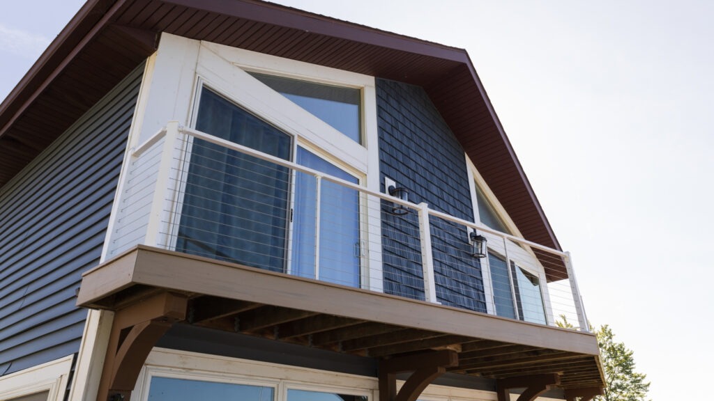 White balcony railing with stainless steel cables and blue siding, modern coastal example of cable deck railing ideas for upper-level decks.