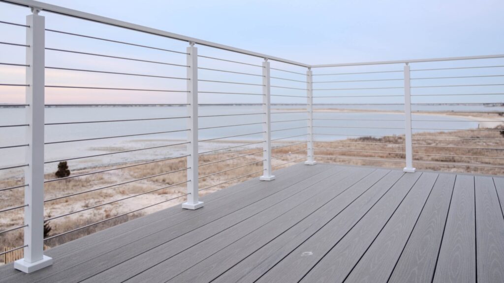 White aluminum cable deck railing with stainless cables and gray composite deck facing ocean.