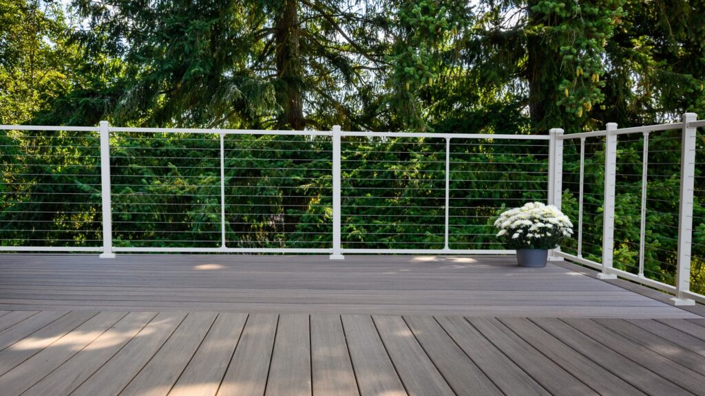 White aluminum horizontal cable deck railing on gray composite deck surrounded by trees.