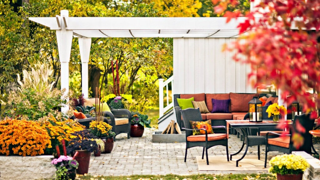 White garden pergola surrounded by colorful fall flowers and wicker patio furniture.