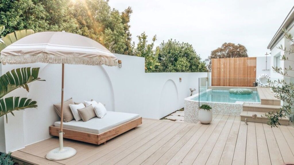 White patio deck with small pool, wooden lounge area, and modern umbrella.