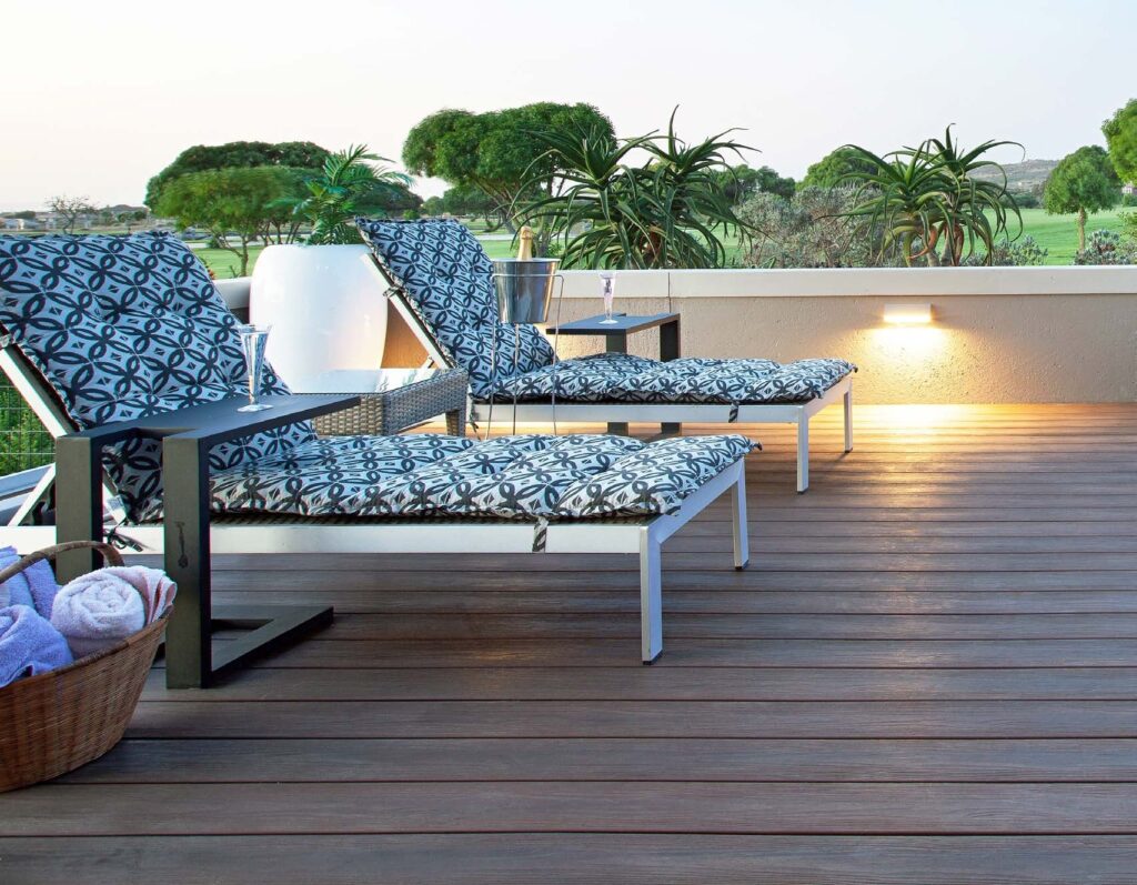 A rooftop lounge area with Eva-Last Eclipse Autumn Mahogany decking, paired with patterned sun loungers and surrounding greenery. Warm lighting highlights the deck’s realistic grain and even color, creating a relaxing outdoor retreat ideal for entertaining or unwinding.