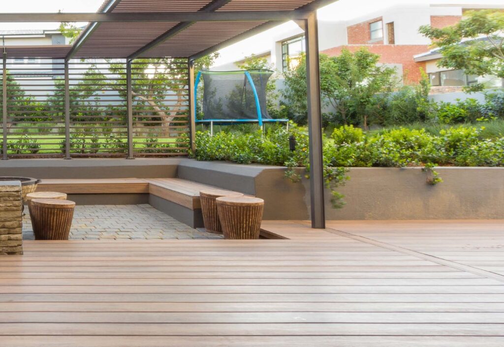 A modern backyard pool area showcasing Eva-Last Eclipse Dockside Brown decking surrounding a bright blue pool with a stone waterfall feature, soft lighting, and lush landscaping.