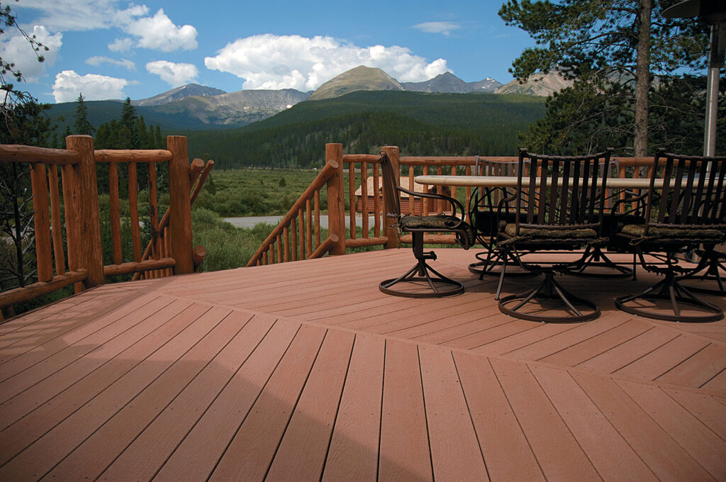 Outdoor deck built with Envision EverGrain Redwood composite decking overlooking a mountain landscape. The warm red-brown boards feature deep, non-repeating woodgrain that adds a natural, rustic look to the space. The deck surface appears solid and well-suited for scenic outdoor living areas.