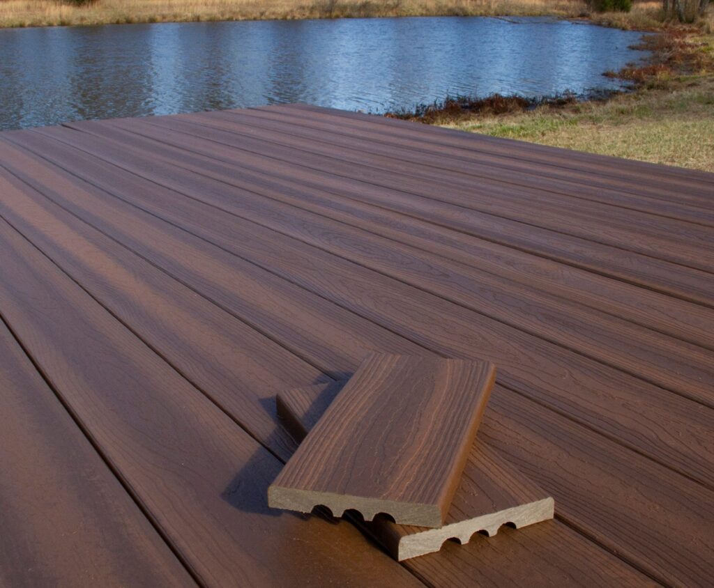 Lakeside deck built with Envision Ridge Premium Black Walnut decking, showcasing dark brown hues and natural grain texture across wide deck boards. The surface appears smooth and uniform, extending toward the water for a clean, modern look. The color complements the natural landscape while maintaining a refined, finished appearance.