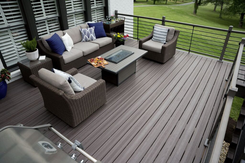 Envision Ridge Premium Gunstock composite decking installed on a modern outdoor deck, featuring wide boards with natural wood grain and warm brown tones surrounding an outdoor seating area.