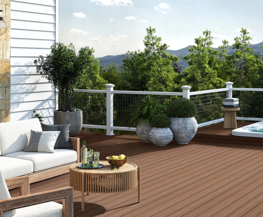 Envision Ridge Premium composite decking in the Sandstone color creates a warm, natural foundation for this elevated outdoor living space. The light brown boards pair seamlessly with modern outdoor furniture, white railing, and lush greenery. The subtle wood-grain texture adds visual depth while maintaining a clean, low-maintenance finish.