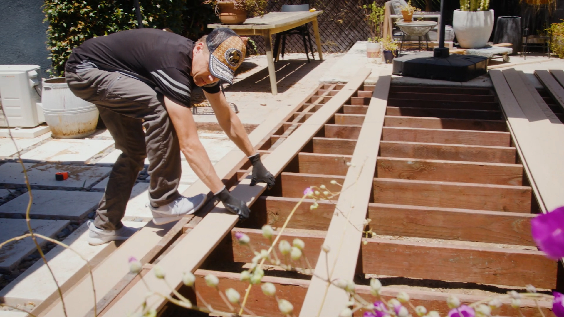 Installer placing composite deck boards across exposed wood joists during deck construction. The image shows proper composite decking support spacing across a framed deck structure before fastening boards in place.