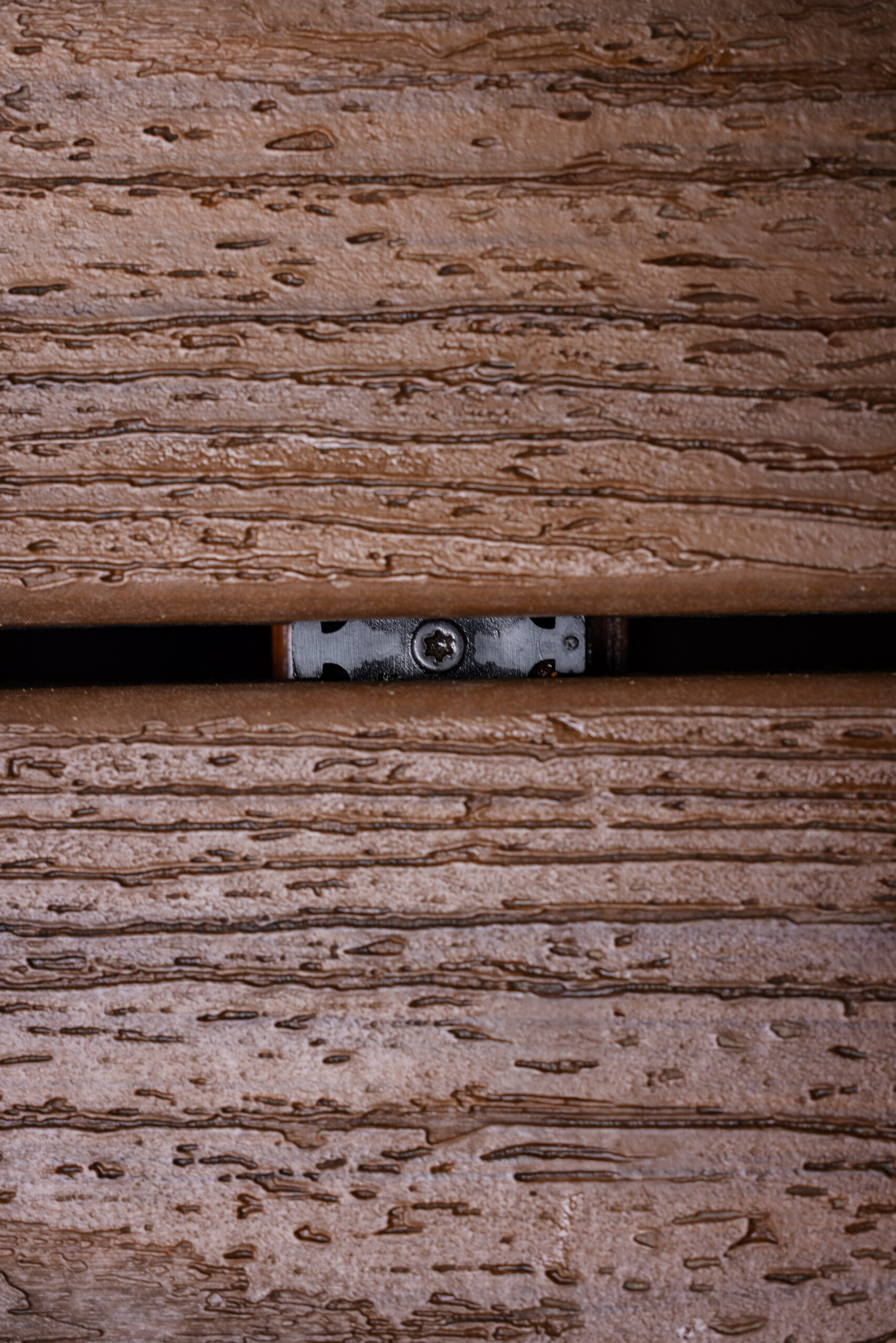 Trex hidden fastener installed between two grooved composite deck boards. The clip sits inside the side grooves, demonstrating how deck fasteners hidden beneath the surface create consistent spacing and a clean finish.