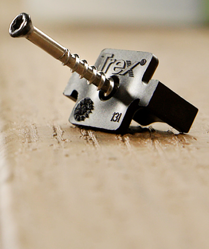 Close-up of a Trex hidden fastener clip with a corrosion-resistant screw attached. The fastener shows the clip design used to secure grooved composite decking boards to the joist without surface screws.
