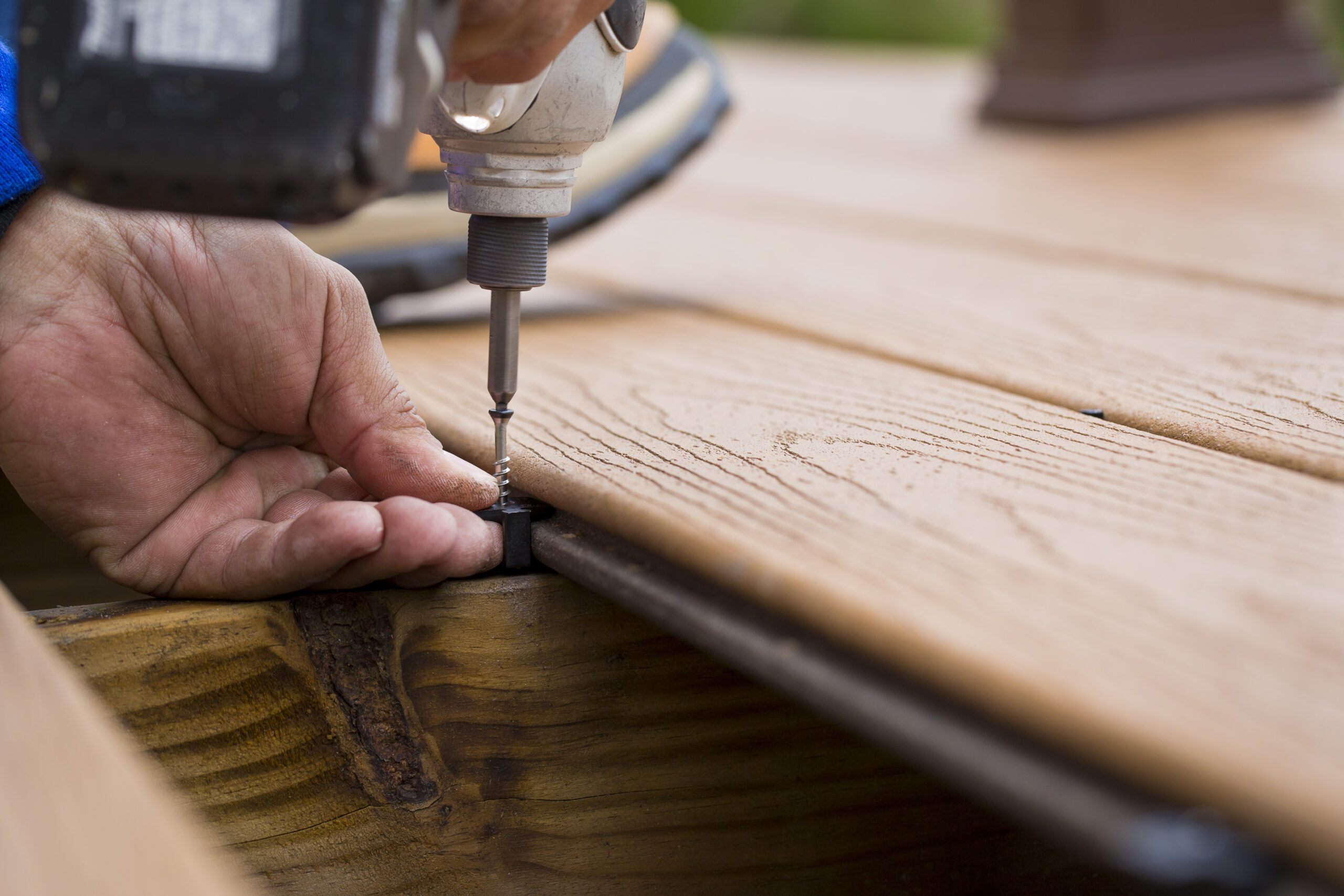 Contractor installing Trex decking with hidden fasteners using a drill to secure the clip into a wooden joist. The image shows how hidden deck fasteners attach boards from the side rather than through the top surface.