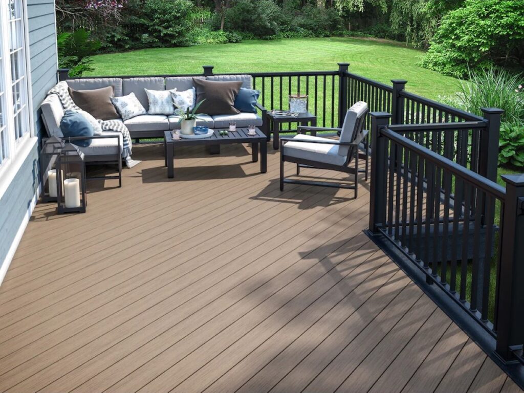 Deckorators Pioneer Coastland Brown decking installed on a backyard deck with black railing and outdoor seating, showcasing a warm brown color and natural wood-look grain.